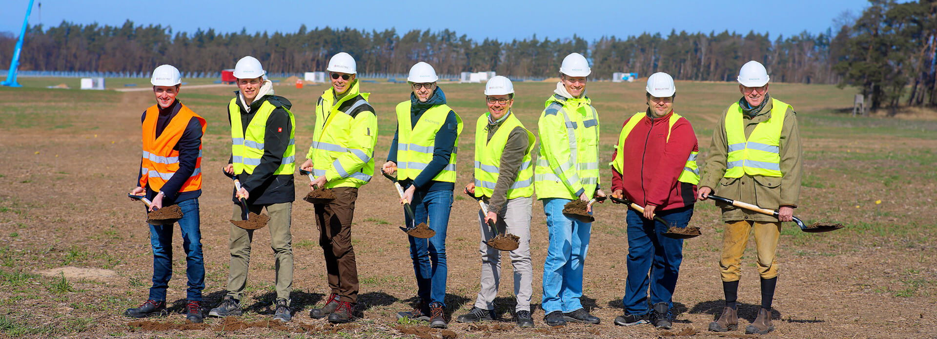 Eight people wearing high-visibility jackets stand on the construction site of the solar farm Borrentin and hold