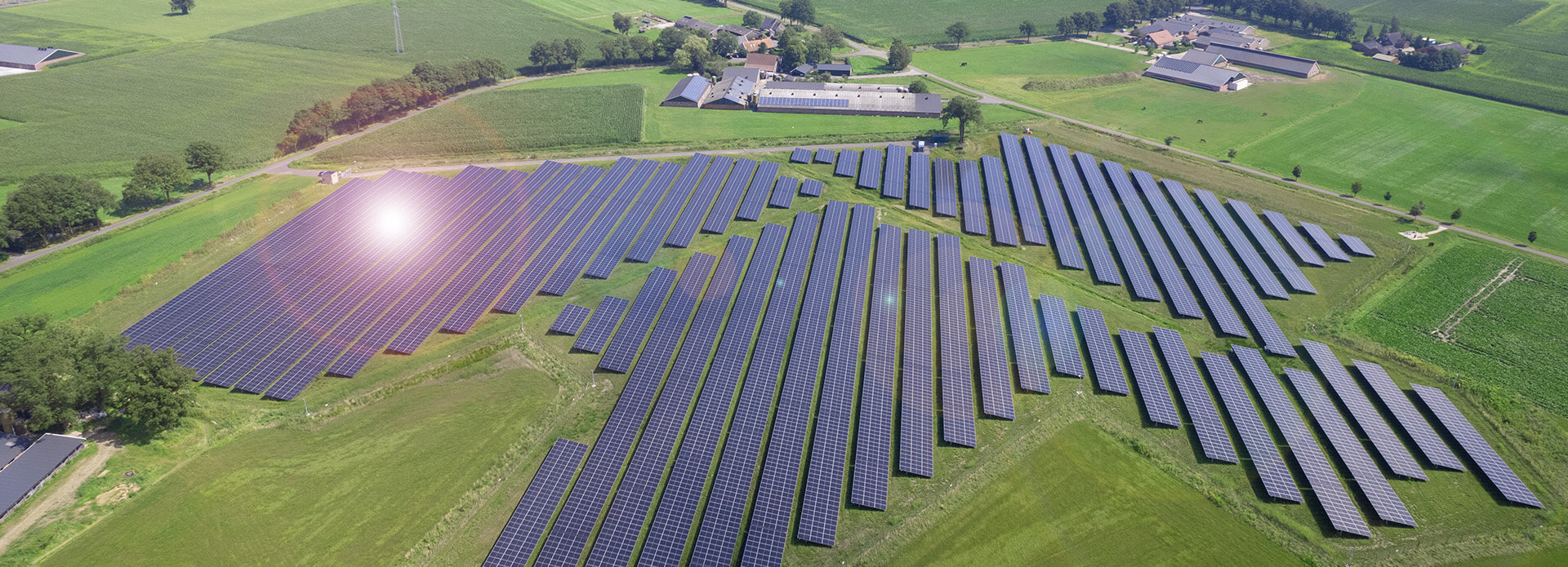 A solar farm with green fields around is seen from above